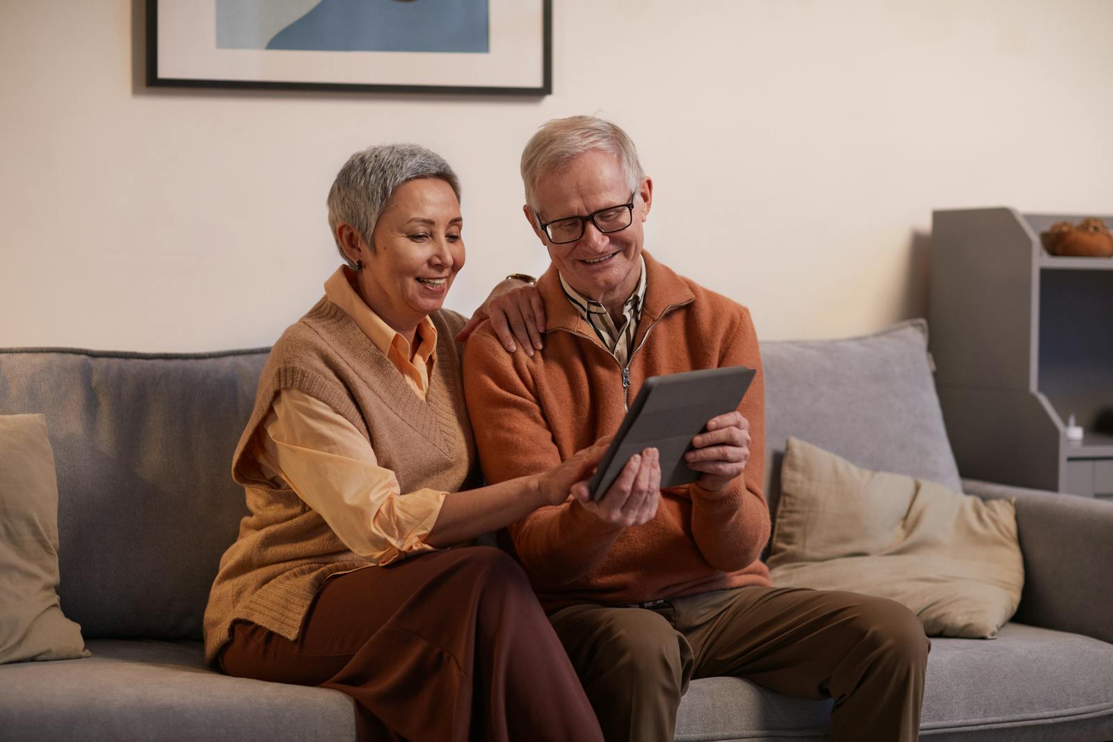 Happy senior couple sitting together on a sofa using a tablet indoors.